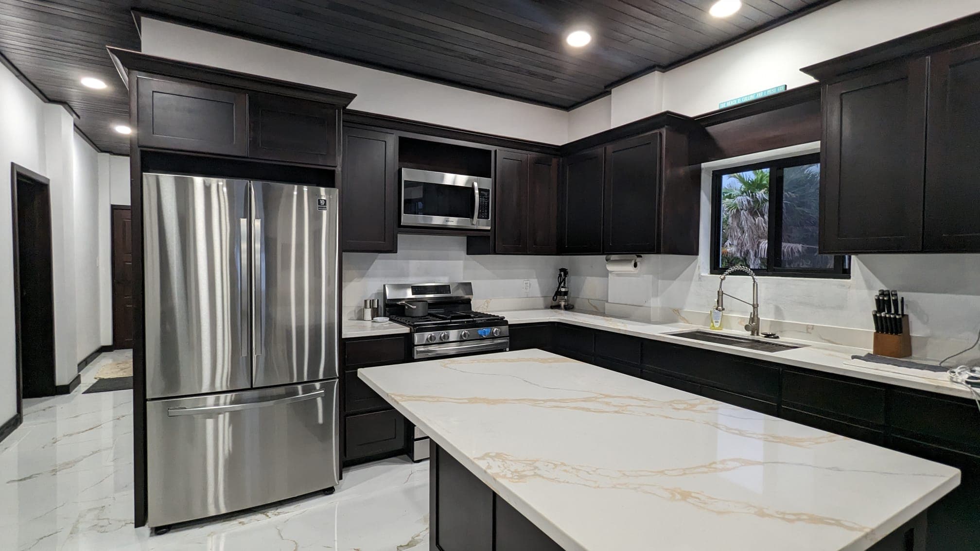 Modern kitchen featuring dark cabinetry, stainless steel appliances, and a white marble countertop.