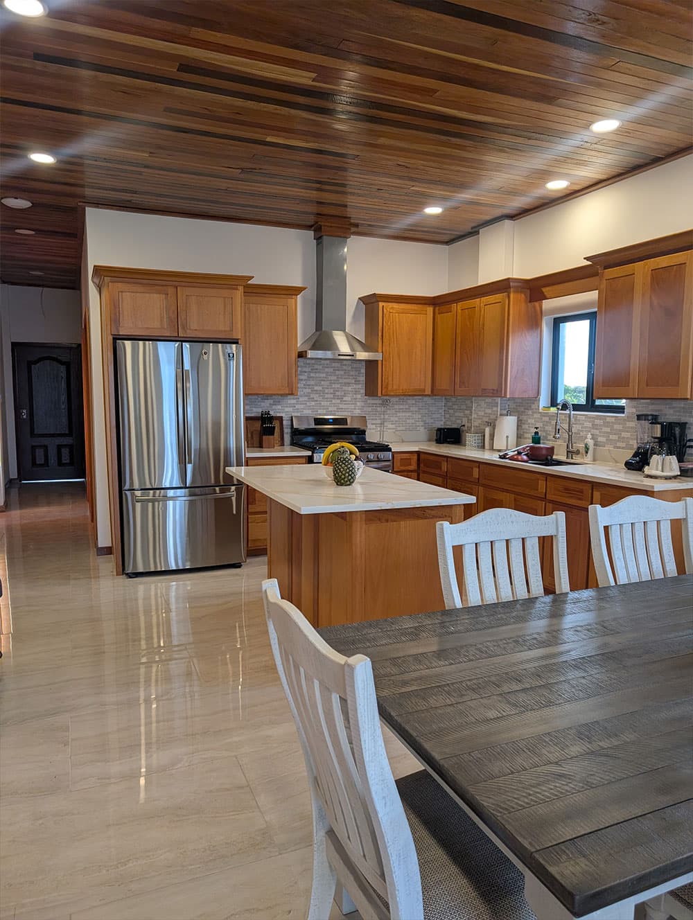 A modern kitchen featuring wooden cabinets, stainless steel appliances, and a dining table with white chairs.