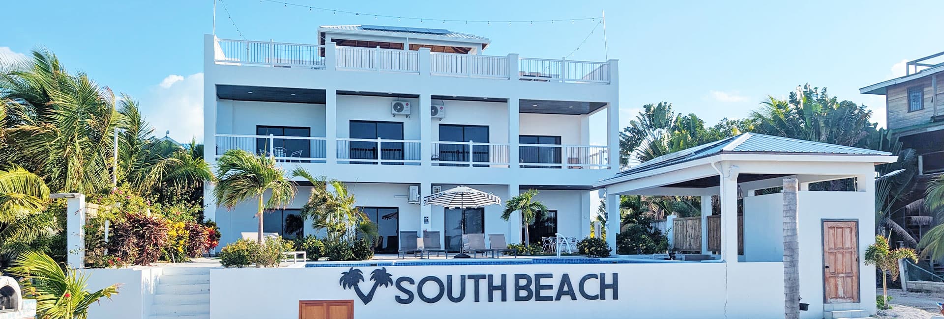 A modern beachfront building labeled "SOUTH BEACH," surrounded by tropical plants and clear blue skies.