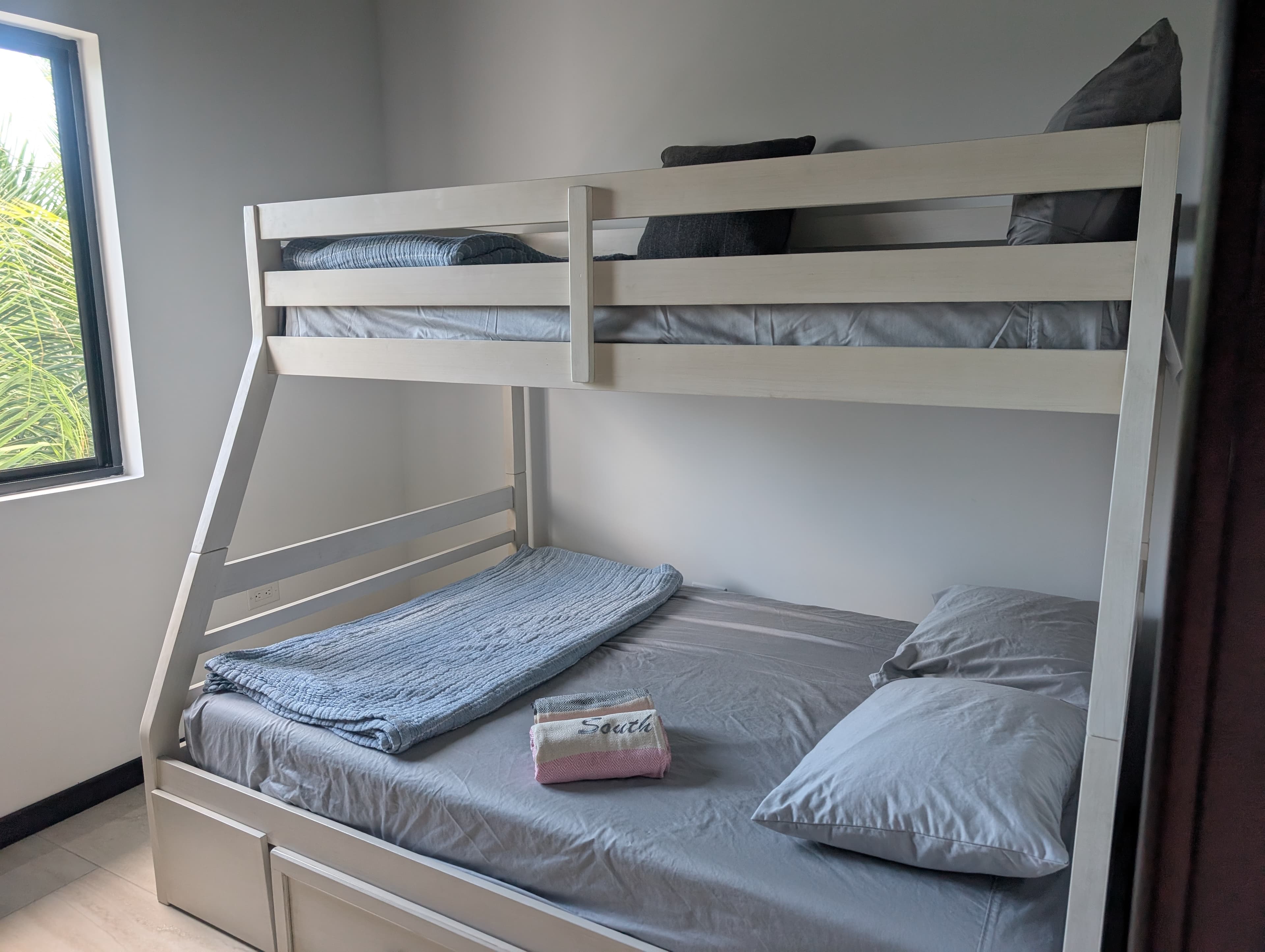 A neatly made bunk bed in a bright room with a large window.