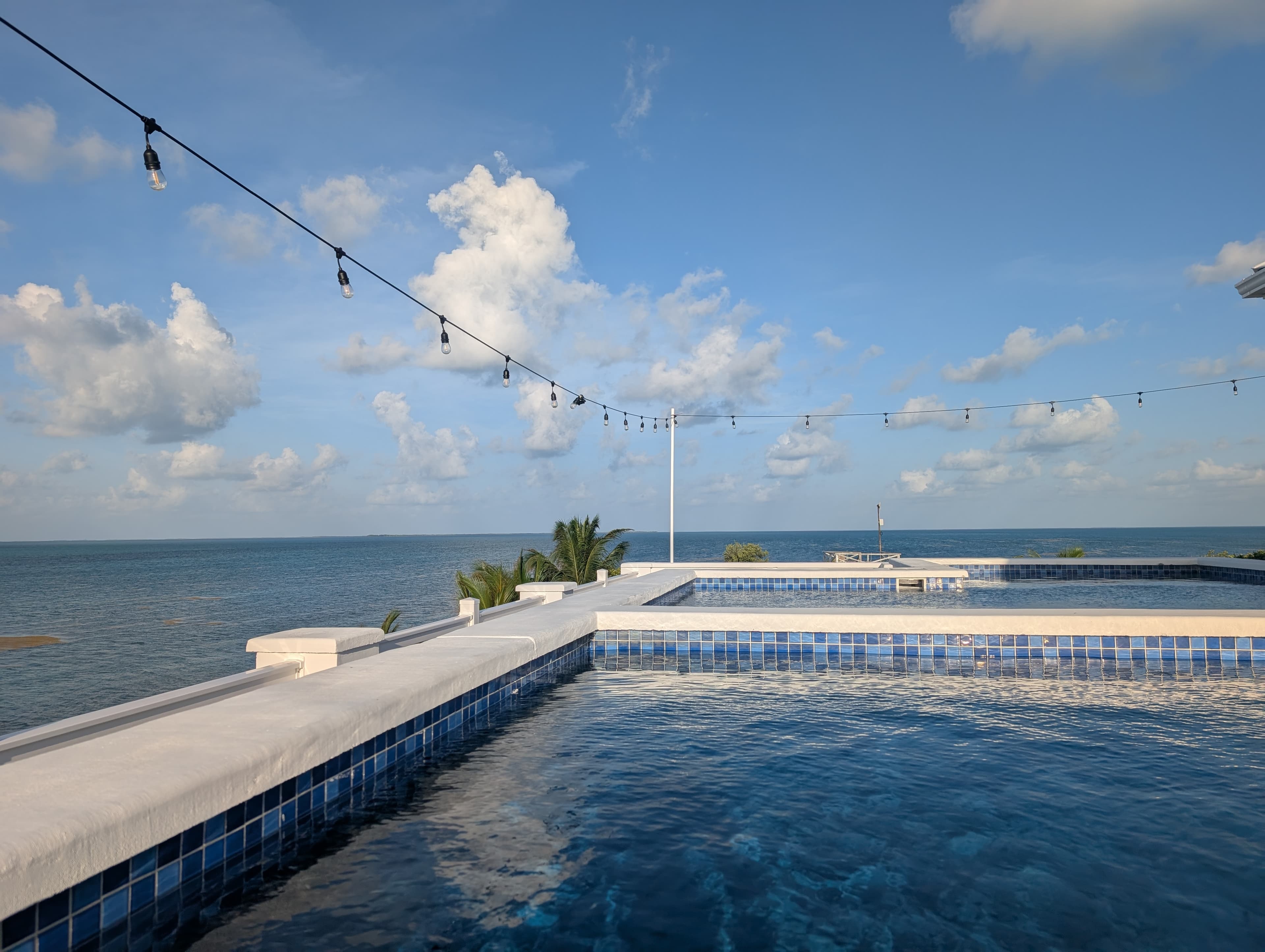 A tranquil pool overlooking the ocean under a partly cloudy sky.