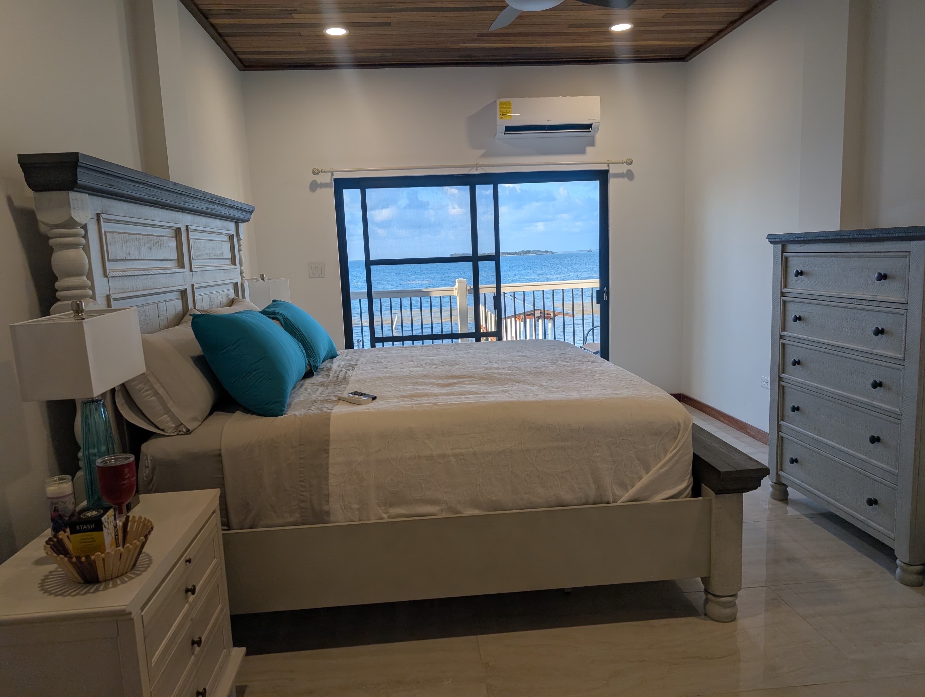A cozy bedroom featuring a large bed, dresser, and a window with a view of the ocean.