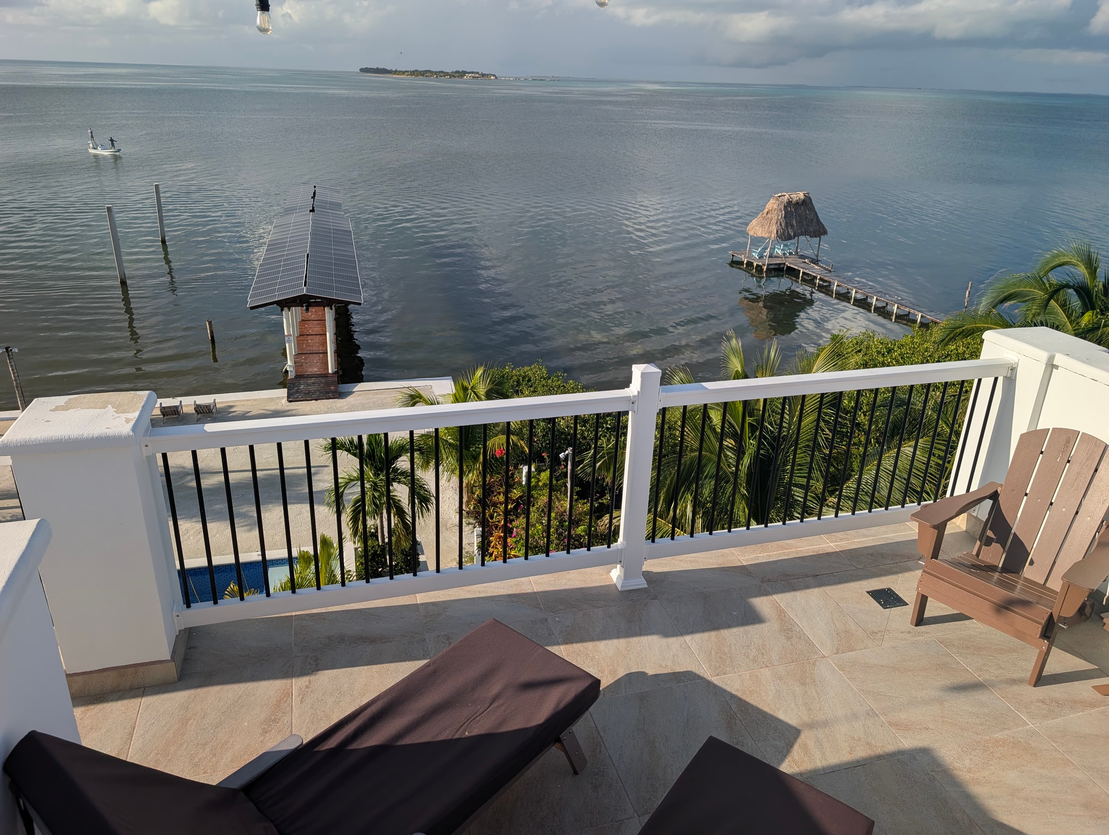 A balcony with two lounge chairs overlooks a calm bay and a distant island.