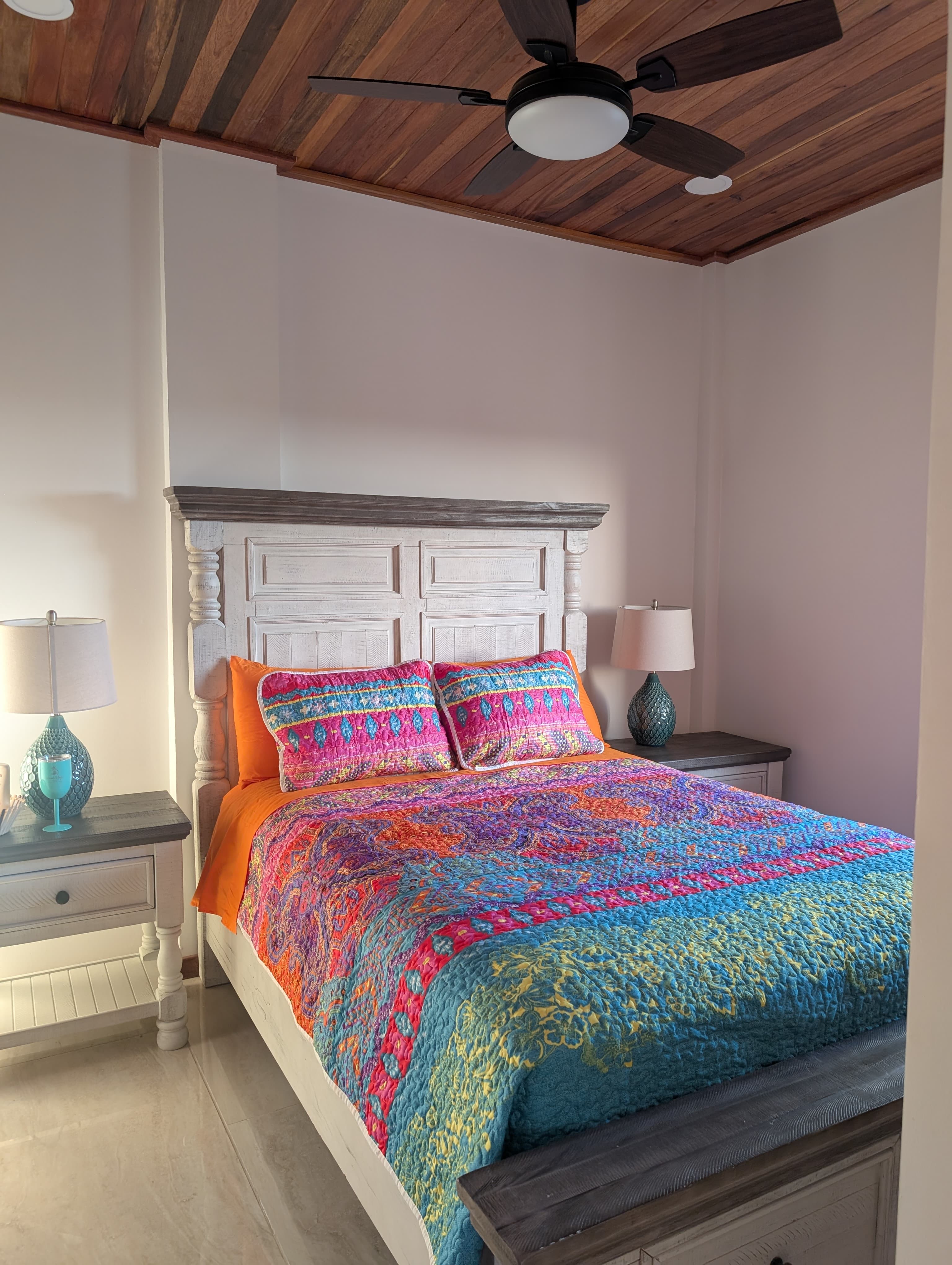 A vibrant bed with a colorful quilt and decorative pillows in a softly lit bedroom.