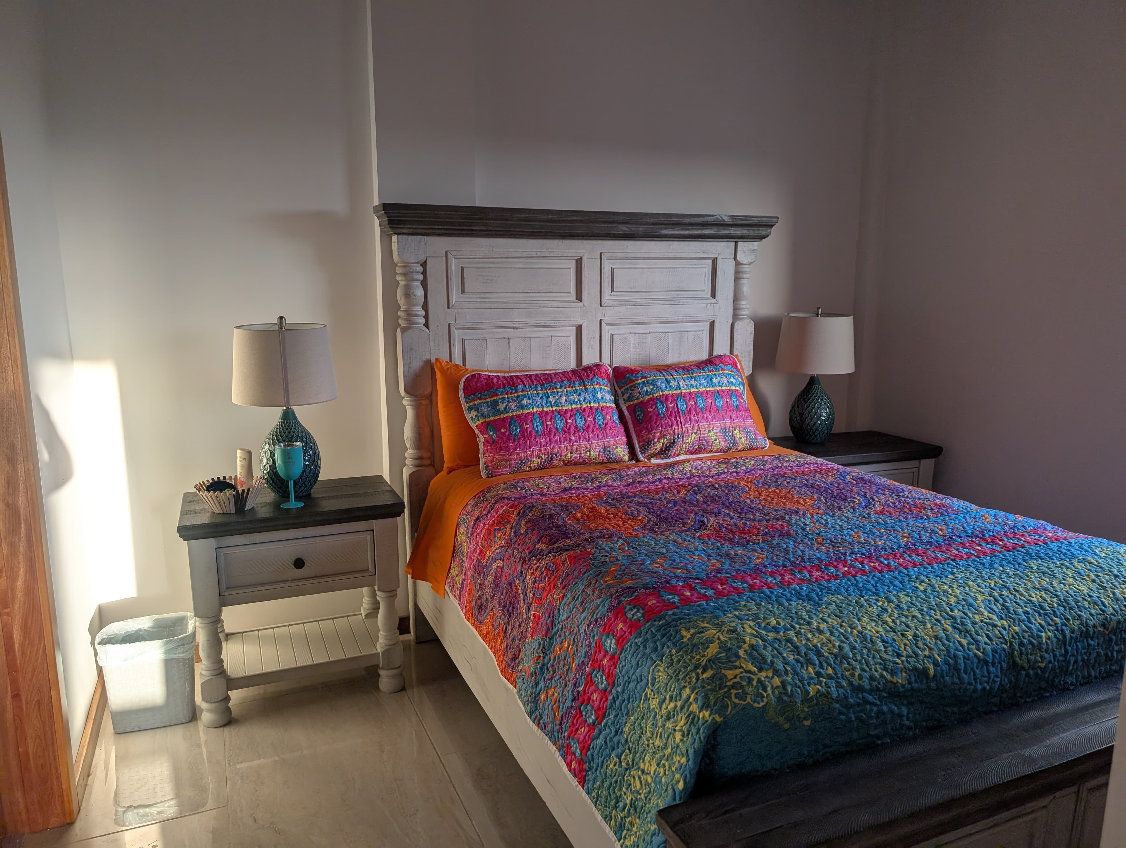 A colorful bedspread adorns a neatly made bed in a well-lit bedroom with bedside tables and lamps.