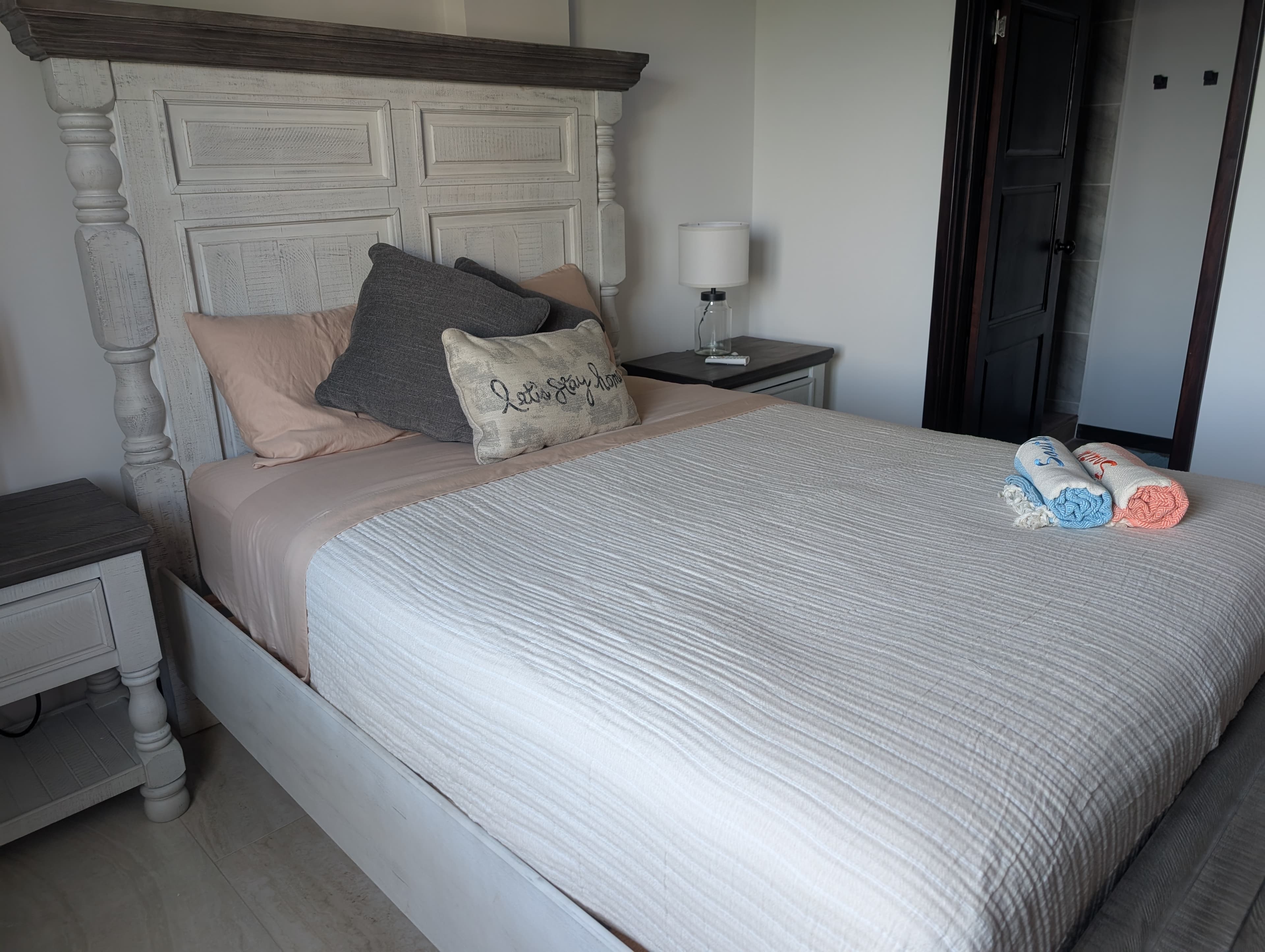 A neatly made bed with a decorative headboard, accompanied by a lamp and neatly folded towels.