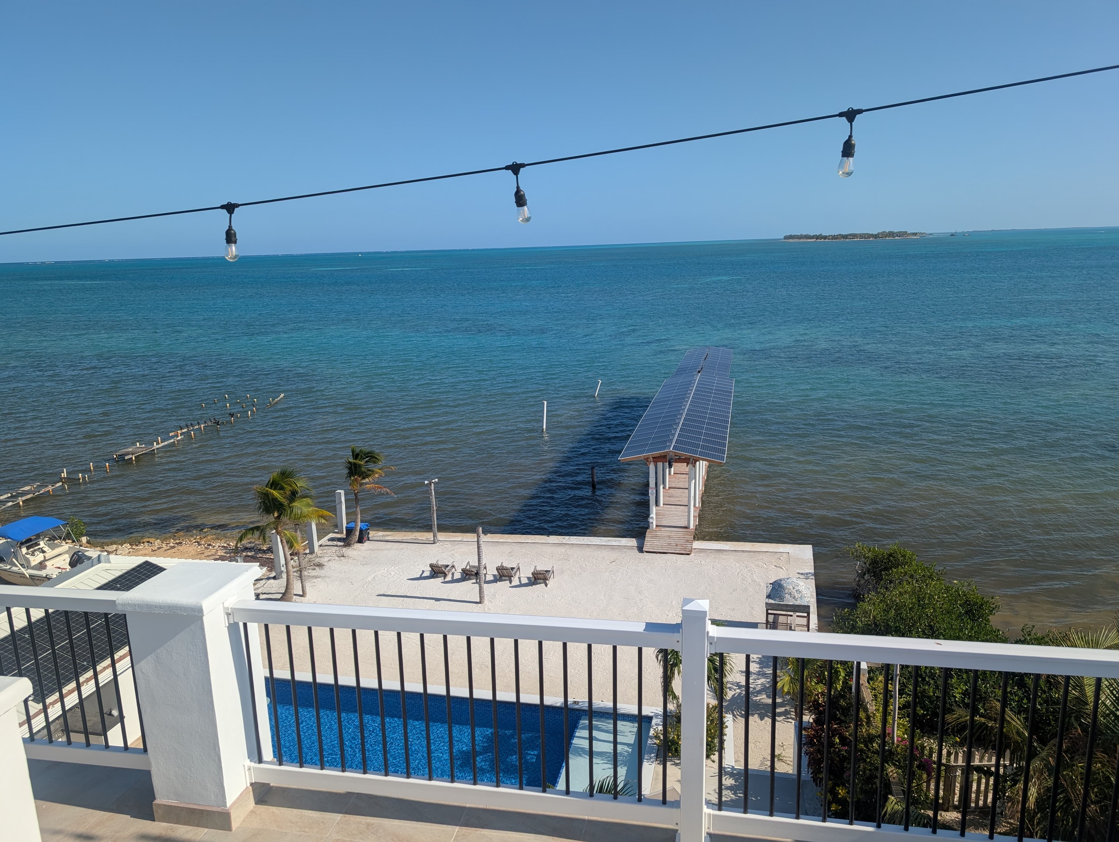 View of a serene waterfront with a dock, pool, and clear blue sky.
