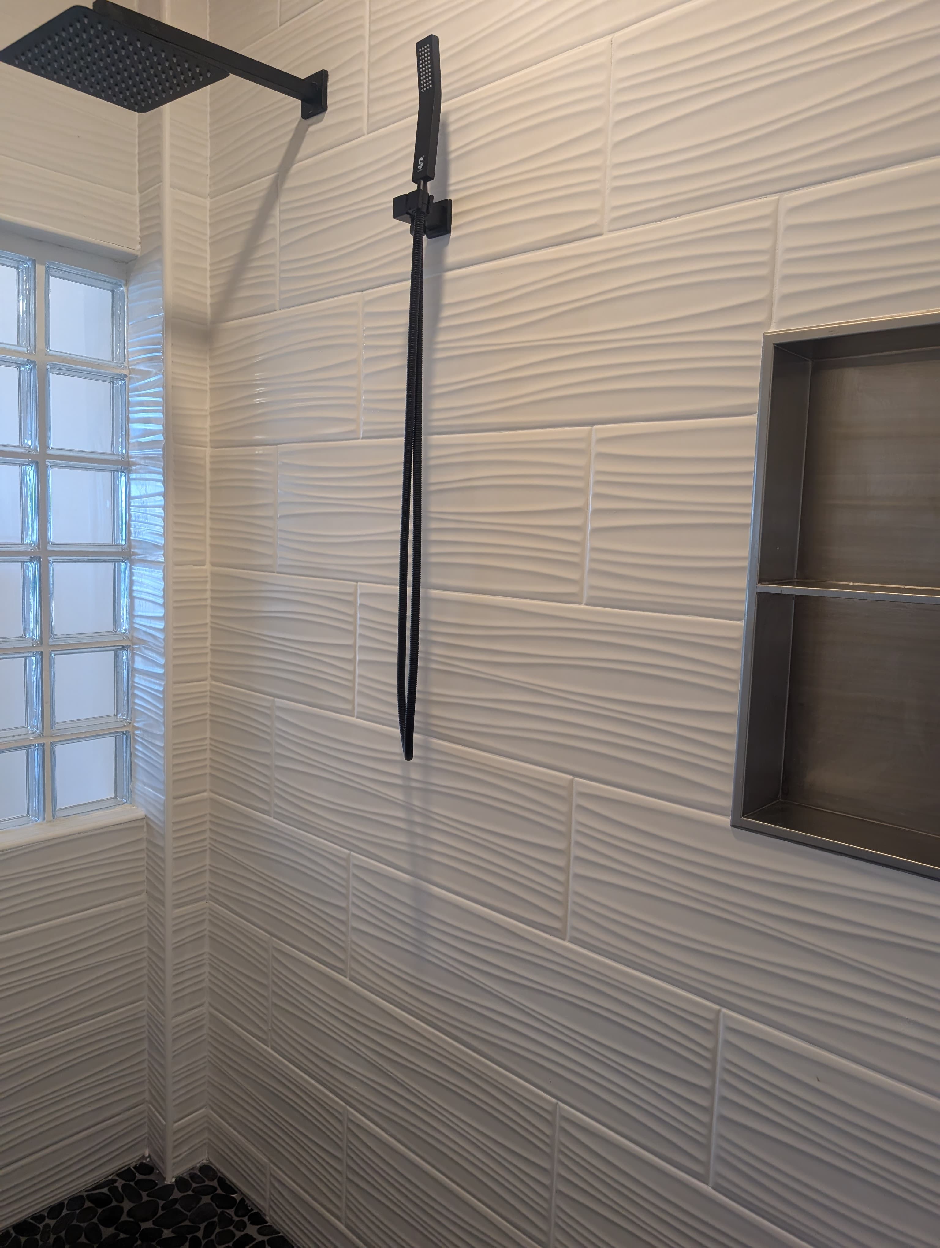 A modern shower wall featuring textured tiles, a rain showerhead, and a sleek black towel holder.