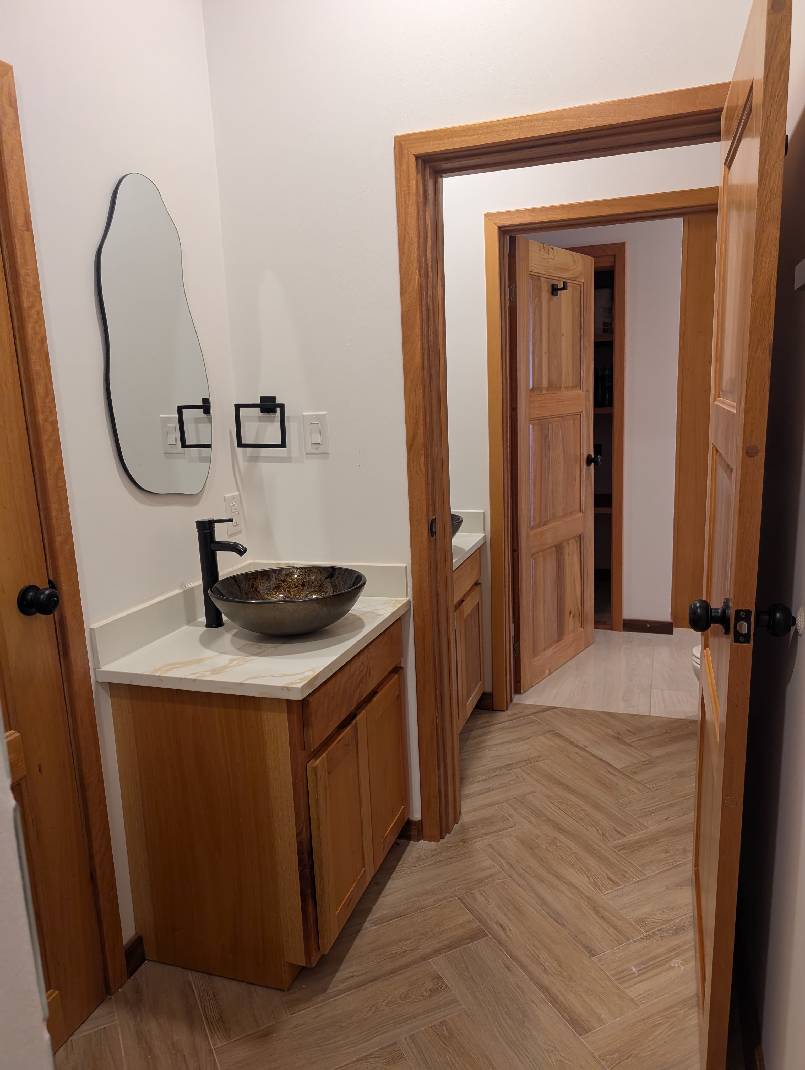 A modern bathroom featuring a wooden vanity, a round bowl sink, and an adjacent wooden door.