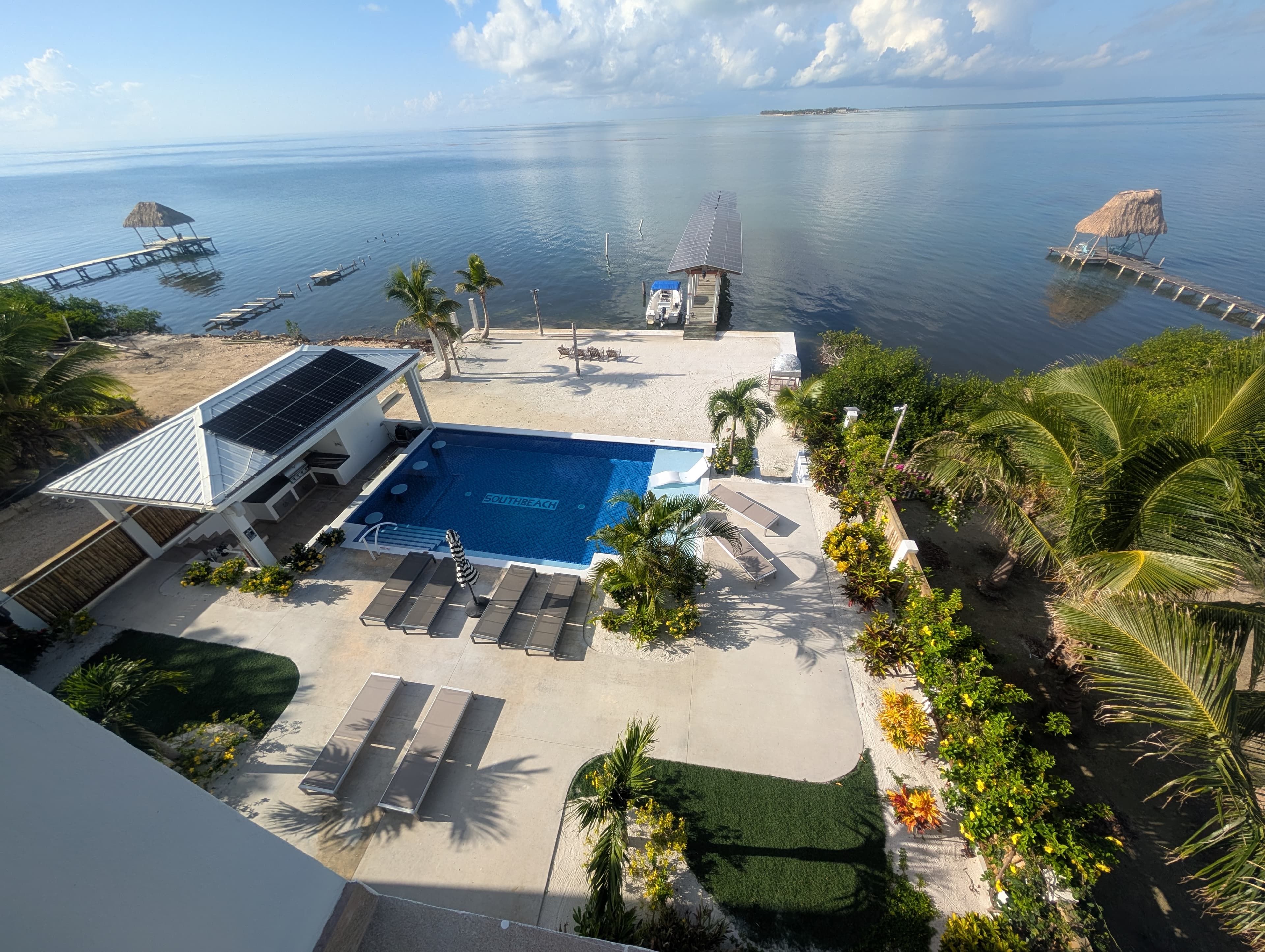 Aerial view of a tropical resort featuring a pool, lounge chairs, and a tranquil ocean backdrop.